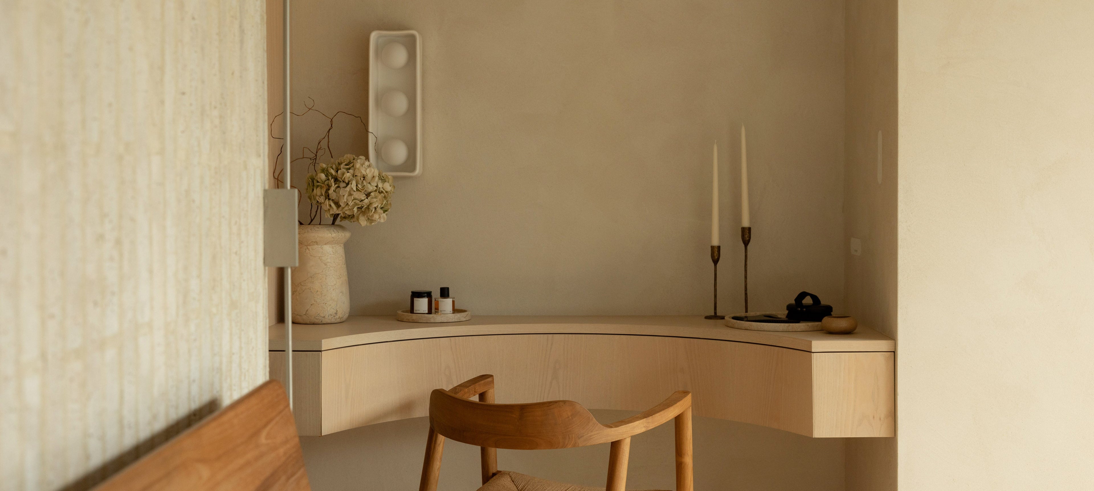 Minimalist interior with a wooden chair and desk against a neutral wall.